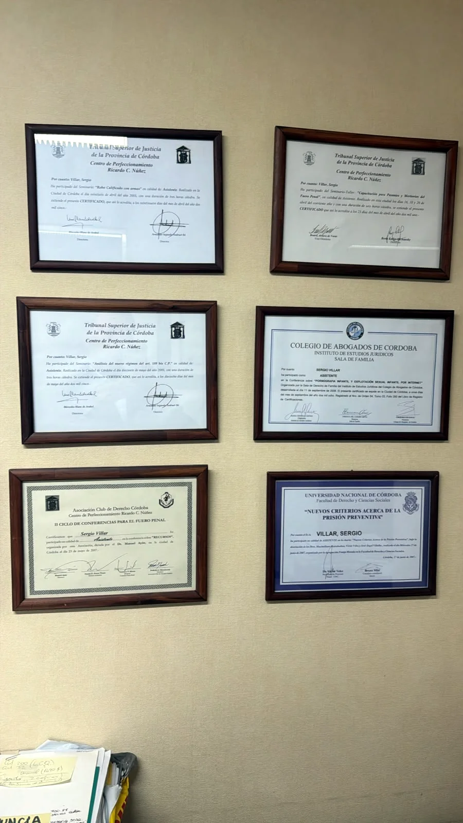 Títulos universitarios y matrícula profesional enmarcados en el despacho